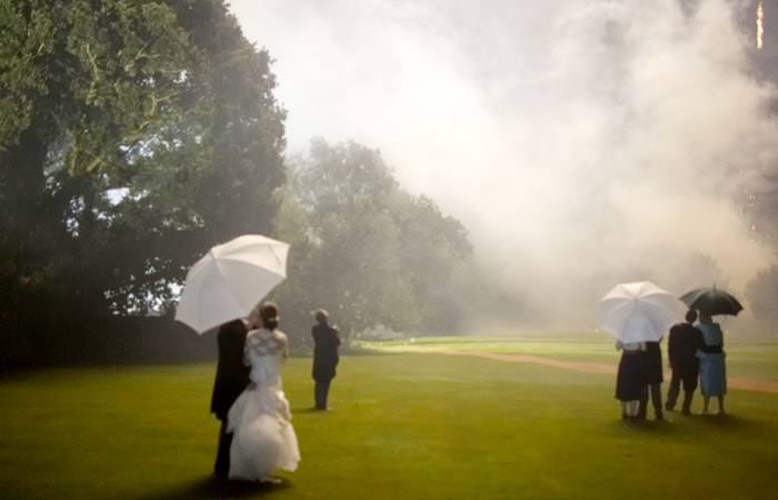 bride and groom watching the fireworks under an umbrella in the rain