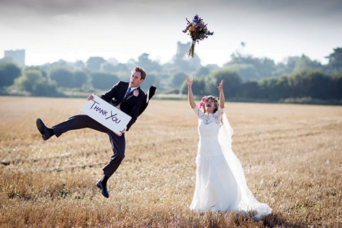 Wedding photograph of couple in field for thank you card holding thank you sign