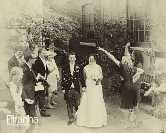 Bride and Groom walking outside chruch with confetti in London - sepia image