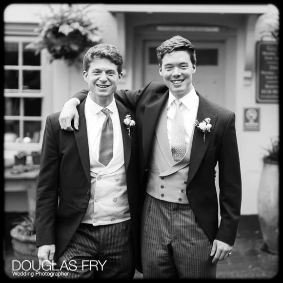 Groom and bestman in black and white in front of pub before wedding