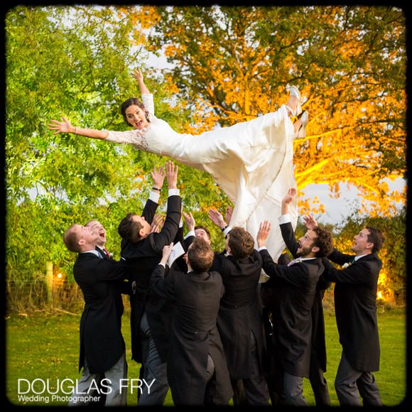 Bride being thrown in air by ushers during photographs