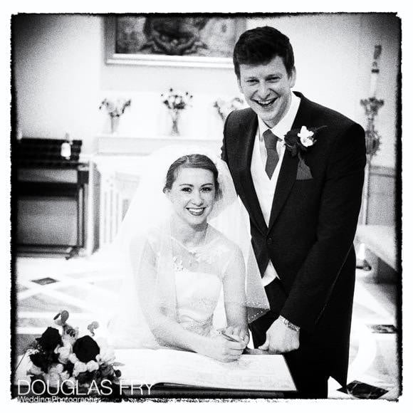 Bride and groom in black and white signing the register in Church