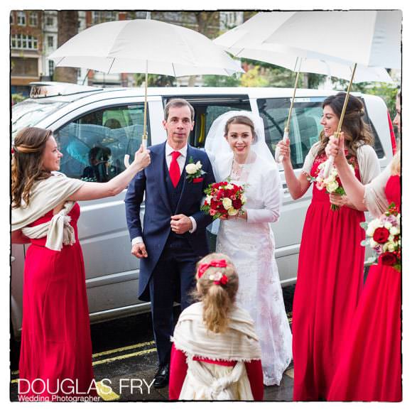 Bride and father arriving at Soho church in London with umbrellas