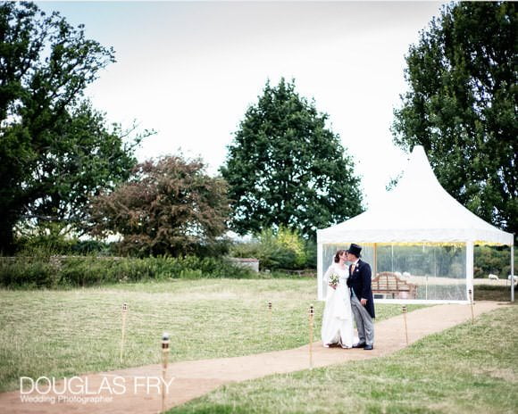 Bride and groom walking in gardens in front of marquee during wedding reception in Oxfordshire