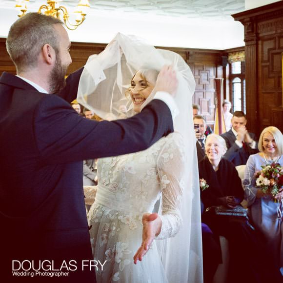 Groom lifting bride's veil during marriage ceremony