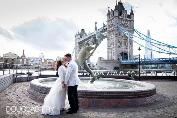 Wedding couple pose next to the boy with dolphin statue next to Tower Bridge