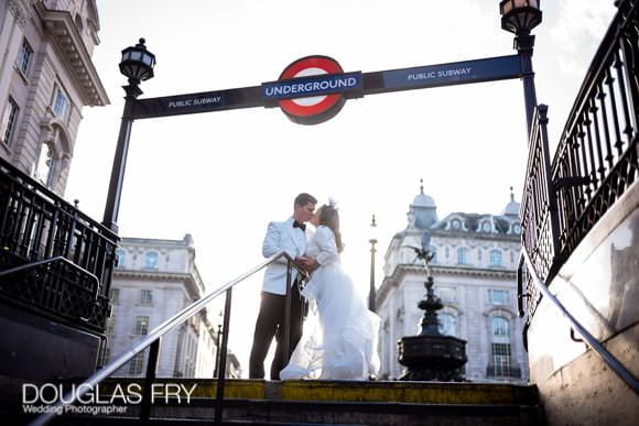 Couple pose for a wedding photograph at Piccadilly Station to include the statue of Eros