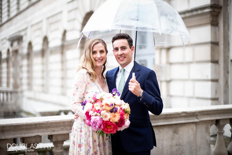 Bride and groom with umbrella in rain at Somerset House