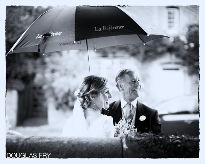 Bride with father of the bride outside church with umbrella