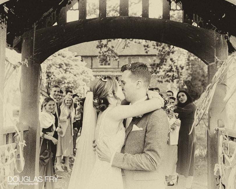 bride and groom kiss at church gate - wedding photograph in black and white