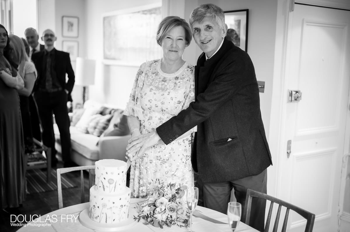 Wedding photography by Douglas Fry of couple cutting cake at home during reception.